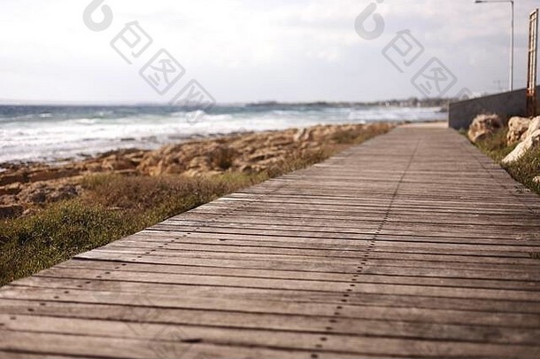 沿着海岸的漂亮的木制人行道。人行道是用老式木板铺成的。海滩背景上的天然木板。