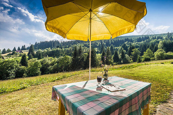 在夏日的山区乡村，一张有桌布和黄色阳伞的桌子