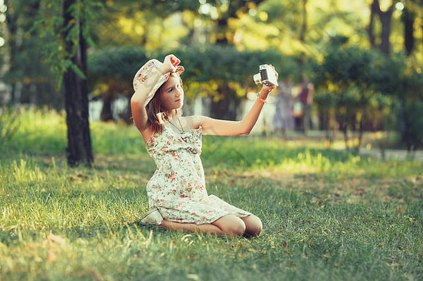 女孩玩<strong>照片</strong>相机坐着草公园自拍拍摄世界