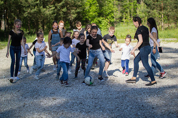 阳光明媚的日子里，一群青少年和一支儿童队在院子里踢足球