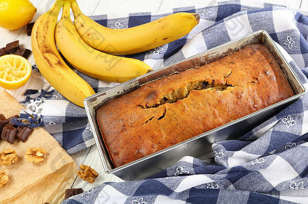 特写镜头：新鲜烤好的美味香蕉面包，核桃和巧克力片放在面包盘中，配上厨房毛巾、熟香蕉和配料