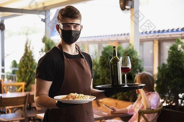 在冠状病毒大流行期间，服务员戴着医用口罩和手套在餐厅工作。代表服务和安全的新常态。点菜、吃饭、喝酒。照顾客户。