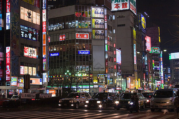 在日本东京新宿，沿着的建筑物上有许多明亮发光的标志，晚上有繁忙的街景