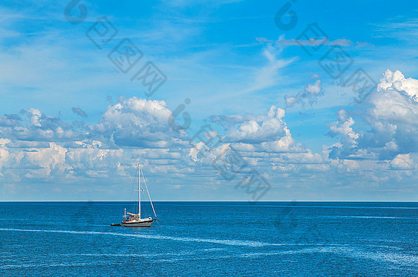 蓝色海洋上孤零零的帆船，碧蓝的天空中有白色蓬松的云朵，看起来宁静、放松、平静、与世隔绝