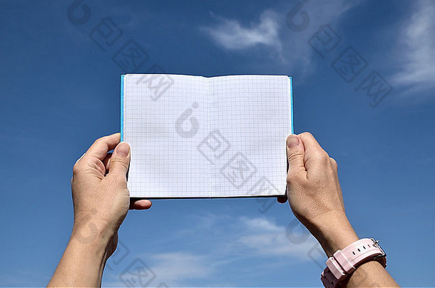 以蓝天为背景，手持方形图案的袖珍笔记本
