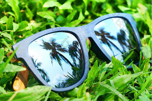 放在草地上的镜头上反射着椰子树的蓝色太阳镜。