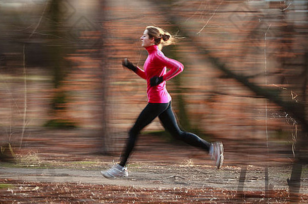 在寒冷的秋冬季节，一位年轻女子在城市公园里跑步