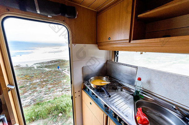 在露营房车上烹饪晚餐或早餐，可欣赏海滩风光。准备鸡蛋，俯瞰西班牙加利西亚的内米尼亚海滩。带着房车、马达旅行