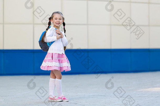 一个穿着夏装、背着背包的漂亮小女孩站在城市的墙边。