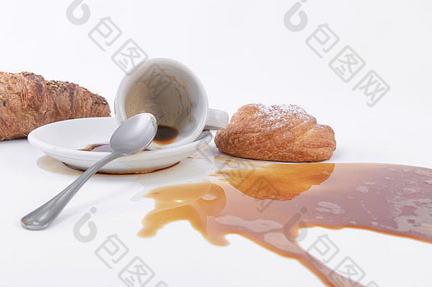 洒出来的咖啡和一卷金色的松饼，上面放着糖粉，背面放着牛角面包。
