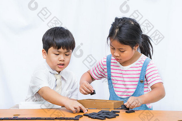 小男孩和漂亮女孩在白色背景的木桌上玩多梅诺，