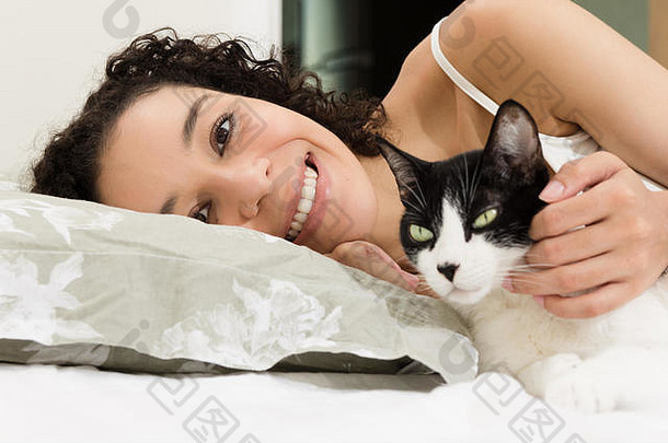 黑人妇女在床上抚摸她可爱的猫的肖像。爱护动物、关爱、宁静的理念。
