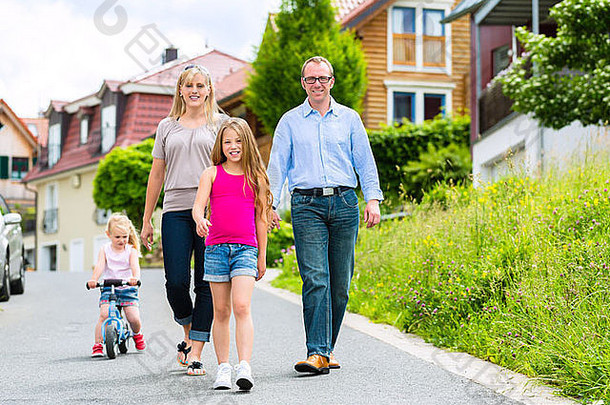 一个年轻的家庭，带着母亲、父亲和女儿穿过一个住宅区，也许他们会去旅行或远足
