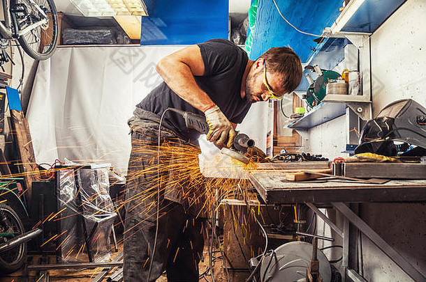 一个身强力壮的男人穿着工作服，在车库的木桌上用金属焊接机焊接，火花四溅