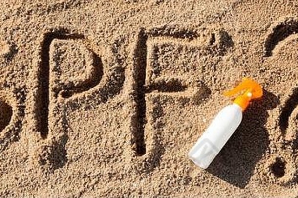 防晒系数。SPF字写在沙子上，白色的瓶子上有防晒霜，上面有问号。皮肤护理概念背景。