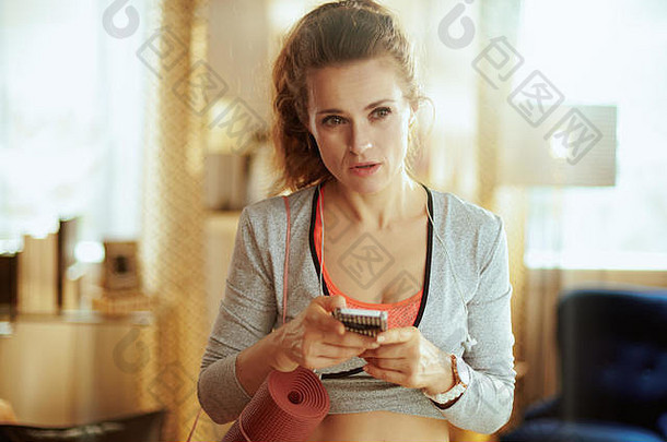 沉思<strong>的</strong>健康<strong>的</strong>女人健身衣服健身席更新健身博客智能手机现代生活房间