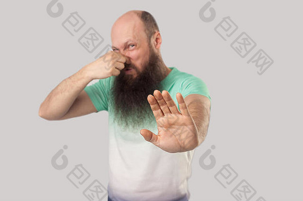 坏气味停止肖像困惑中间岁的秃男人。长胡子光绿色t恤站阻塞鼻子显示停止手势