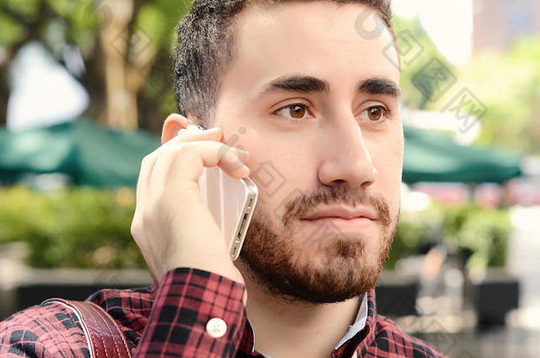 年轻的拉丁男子在电话里讲话的肖像。在户外城市景观。