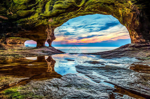 太阳落在苏必利尔湖（Lake Superior）上，这张照片拍摄于密歇根州上半岛一段岩石海岸上的一个海洞。