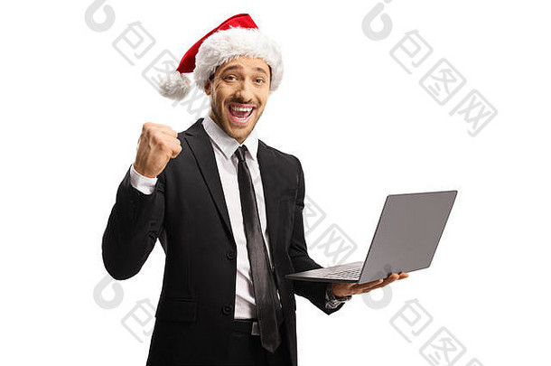 年轻的职业男子穿着西装，戴着圣诞老人帽，打着幸福的手势，手里拿着一台白色背景的笔记本电脑