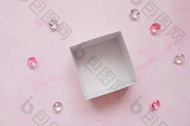 一个白色的空盒子，周围散落着人造粉色和透明宝石，背景为粉色。