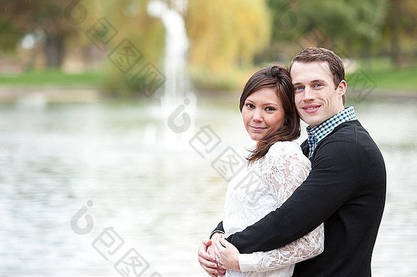 阳光明媚的日子里，一对迷人的年轻夫妇在池塘边摆姿势。