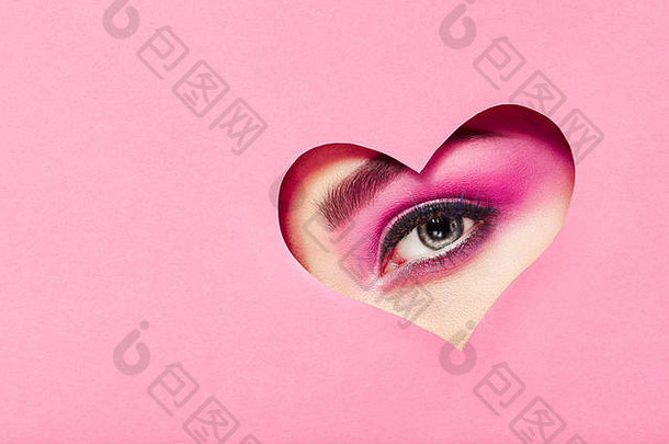 情人节的概念照片。节日粉色妆容女孩的眼睛。粉红色背景上的纸心。情人节