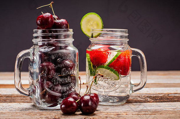 木桌上放着两罐装着新鲜樱桃和水果的水。