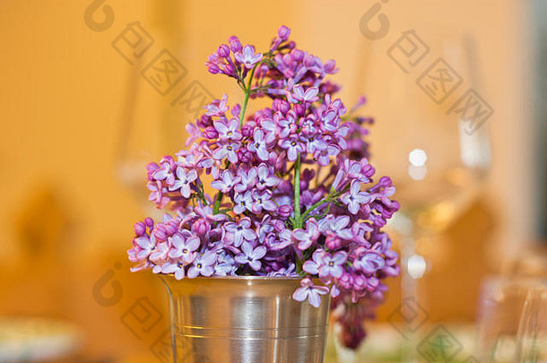 背景是酒杯，桌子上的金属杯里放着丁香花，像春天的花束。温暖的色调搭配舒适的内饰。