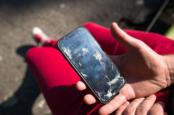 智能手机破损，玻璃、屏幕上有裂缝。年轻人手里拿着电话，既失望又悲伤。愤怒、愤怒和acci的概念