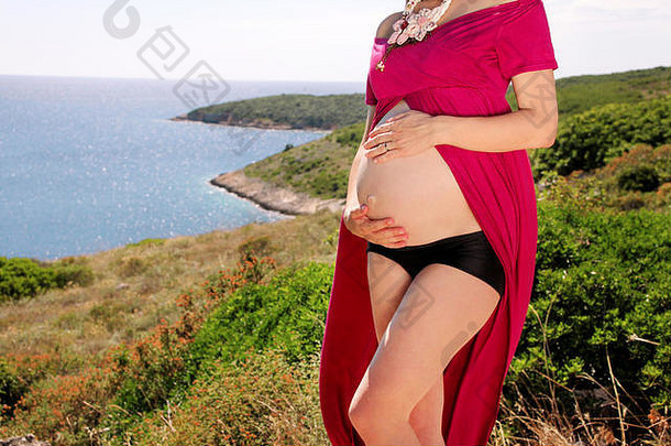 美丽的孕妇和女士站在自然环境中，抱着她怀孕的肚子。在等孩子。妈妈牵着贝尔的手
