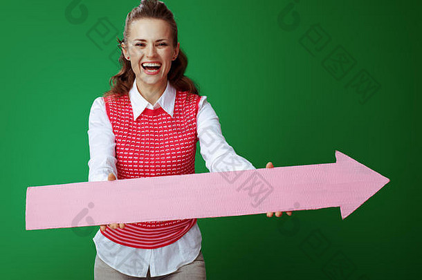 快乐适合学习者女人灰色牛仔裤粉红色的无袖衬衫给大粉红色的箭头指出孤立的绿色背景