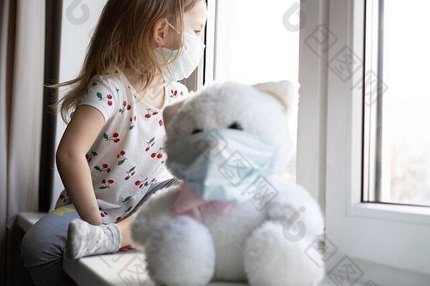 悲伤的孩子和他的泰迪熊都戴着防护面具。儿童与疾病新冠肺炎2019年疾病概念