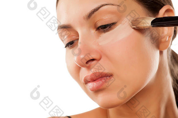 年轻的女人应用液体遮瑕膏眼睛刷