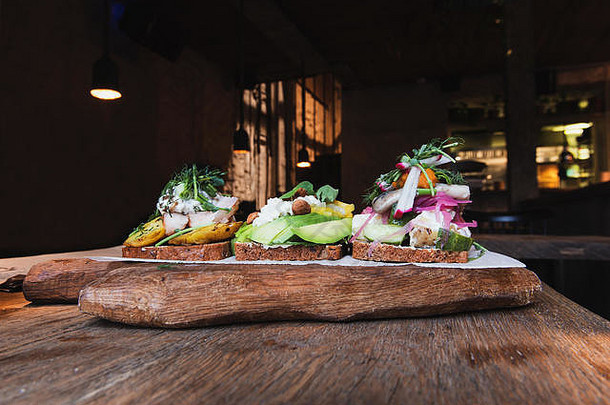 斯堪的纳维亚开胃菜，木制桌子上放着面包，在时髦的咖啡馆里放着木制食物板。用鳄梨、奶酪、杏仁、鲱鱼、土豆和土豆做成的食物