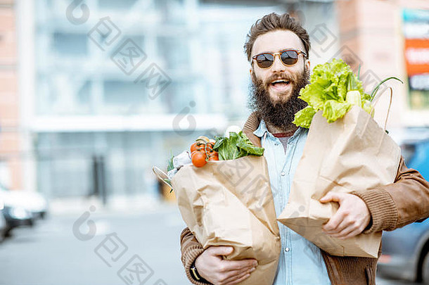 在超市附近的户外，快乐时尚的男人拿着装满新鲜健康食物的购物袋