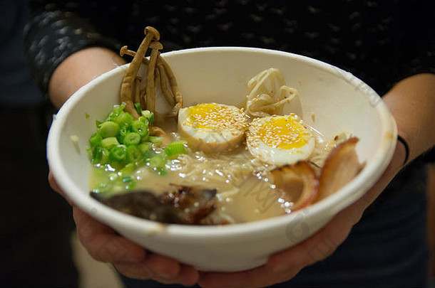 女人手拿着一碗传统的日本猪肉拉面汤，里面有香菇、煮鸡蛋、葱、海藻和猪肉