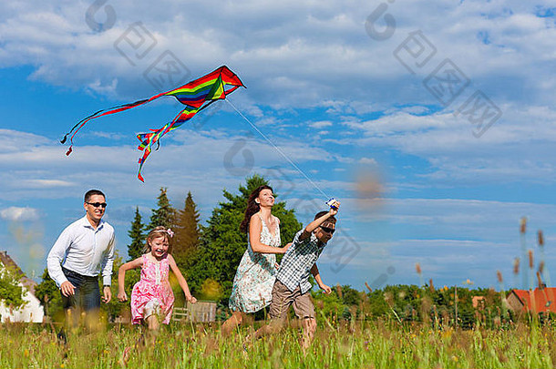 快乐家庭妈妈。父亲孩子们运行绿色草地夏天飞风筝
