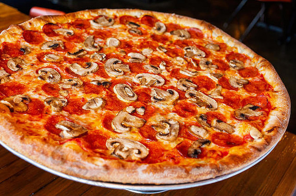 热的大辣香肠披萨美味的披萨，黑底上有融化的奶酪培根番茄火腿辣椒粉蒸汽烟雾