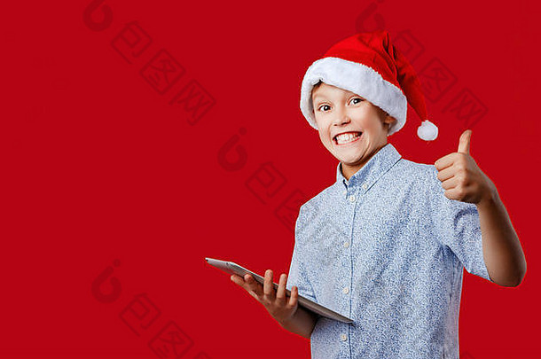 年轻的圣诞老人男孩使拇指手势持有平板电脑