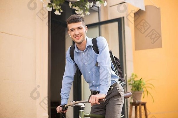 年轻的美丽的男人。蓝色的衬衫无线耳机背包骑<strong>自行车</strong>幸福的相机户外