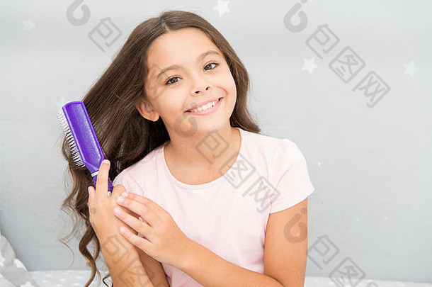 护发<strong>素面</strong>具有机石油梳子头发美沙龙提示女孩长卷曲的头发灰色室内背景孩子卷曲的发型持有毛刷梳子应用石油梳理头发健康的头发