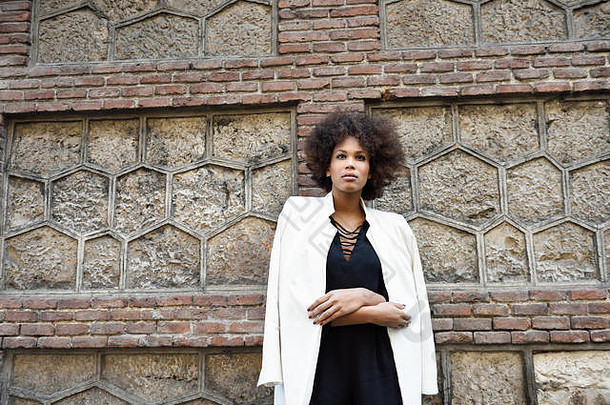年轻的黑色的女人非洲式发型发型站城市背景混合女孩穿白色夹克夹克黑色的衣服摆姿势砖墙