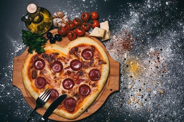 披萨心形状的意大利辣香肠西红柿马苏里拉奶酪大蒜欧芹黑色的背景