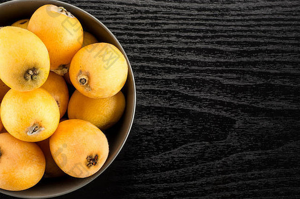 新鲜的橙色日本枇杷灰色陶瓷碗平铺孤立的黑色的木背景