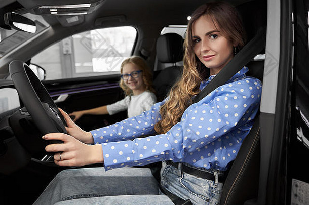 一边视图有吸引力的女人坐着座位司机保持手轮相机微笑汽车沙龙妈妈。漂亮的女儿测试汽车展厅概念购买