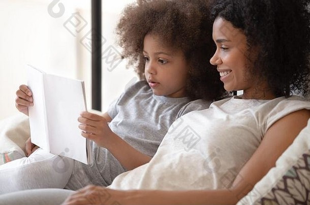 床上非洲女儿<strong>阅读</strong>书妈妈。特写镜头视图