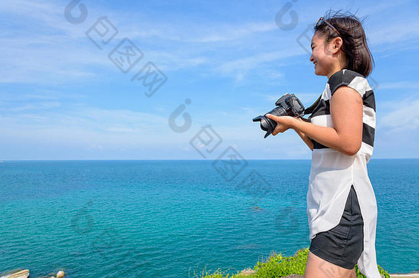 十几岁的女孩持有数码单反相机相机微笑幸福的前岛美丽的自然景观蓝色的海夏天天空