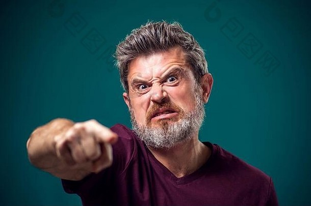 肖像愤怒的有胡子的男人。红色的t恤指出手指相机人情绪概念