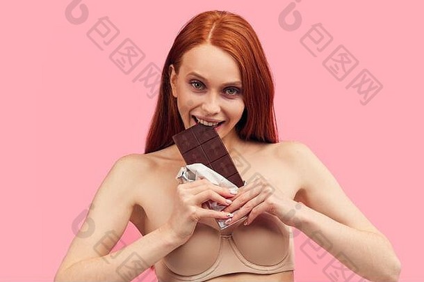 快乐年轻的瘦女人疲惫严重的饮食持有巧克力酒吧摆姿势孤立的粉红色的饮食失败憔悴的红色头发的人女人吃